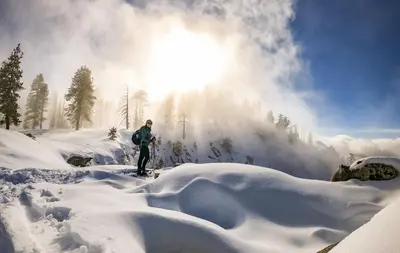 a person standing in the snow with the sun in the background at Oak Retreat by Yosemite National Park in Coarsegold