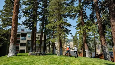 two people riding bikes in front of a building with trees at Spectacular 3 Bedroom Townhome with Pool in Mammoth Lakes