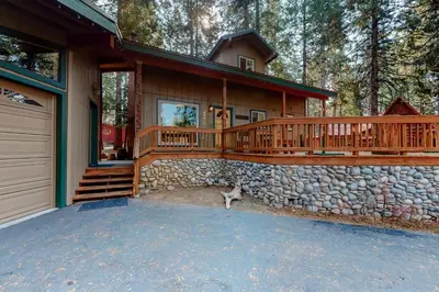 a home with a large deck and a stone wall at Williams Cabin in Shaver Lake