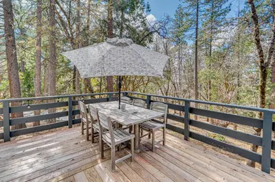 a table and chairs on a deck with an umbrella at Balcony and Forest Views Cabin in Pioneer! in Pioneer
