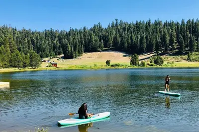 two people are sitting on surfboards in a lake at High Sierra Retreat with a view of Pinecrest lake in Pinecrest