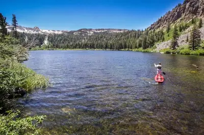 a person is standing on a paddle board in a river at Mammoth Ski & Racquet 20 in Mammoth Lakes