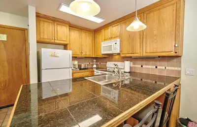 a kitchen with wooden cabinets and a white refrigerator at St Anton Condos with Rec Center in Mammoth Lakes