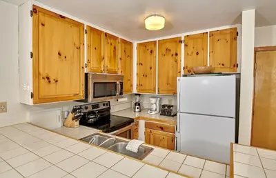 a kitchen with wooden cabinets and a white refrigerator at St Anton Wooded View 2-Bedroom Condos with Ski Lockers in Mammoth Lakes