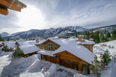 a house covered in snow with mountains in the background at Three-Bedroom Townhouse in Mammoth Lakes