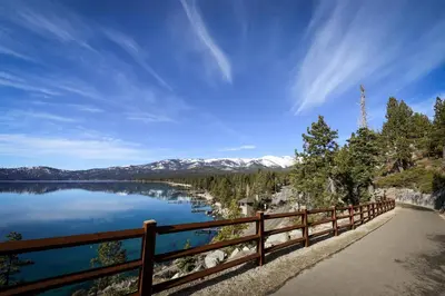 a wooden fence next to a lake with snow covered mountains at Peace Among the Pines in Incline Village