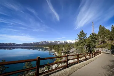a wooden fence next to a lake with snow covered mountains at North Tahoe Nest in Incline Village