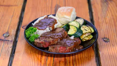 a plate of meat and vegetables on a wooden table at Genas's Sierra Inn & Restaurant in Dunlap