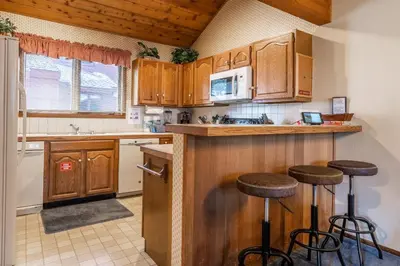 a kitchen with wooden cabinets and bar stools at Spacious Winterset 26 2 Bedrm Plus Loft 3 Full Bathrm Townhome Sleeps 8 Steps to Free Town Shuttle in Mammoth Lakes