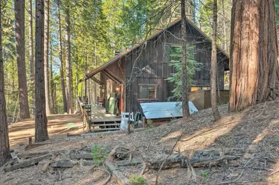 a log cabin in the woods with a bench in front at Walk Downtown Arnold Cabin with Large Deck! in Arnold
