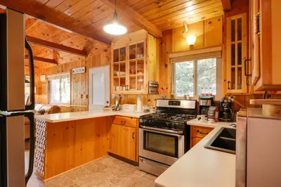 a kitchen with wooden cabinets and a stove top oven at 3 Mi to Big Trees State Park Cabin with Scenic Deck in Arnold