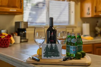 a bottle of wine and two wine glasses on a counter at Lazy Squirrel - Cozy Family House with Full Game Room in Kernville