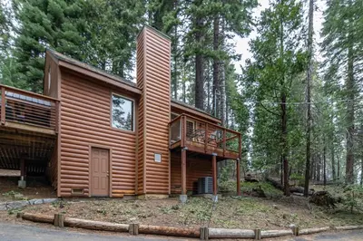a log cabin in the woods with a deck at Yosemite Silvertip Lodge in Fish Camp