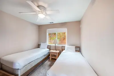 two beds in a room with a ceiling fan and a window at Robinson Shoreline House in Bass Lake