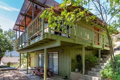 a green house with a balcony and a table at Miglin Lakeview in Bass Lake
