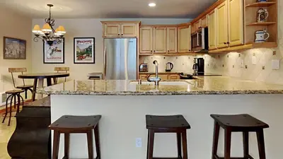 a kitchen with a counter with stools and a refrigerator at Spacious One Bedroom Condo in Mammoth! Free Assigned Parking - Snowbird 107 in Mammoth Lakes