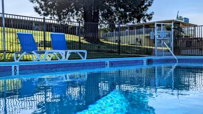 a swimming pool with two blue chairs next to a fence at Foothills Motel in Auburn