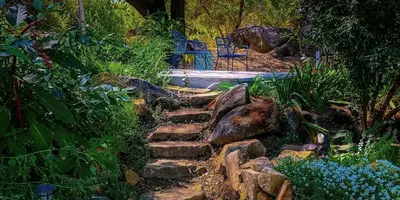 a stone path in a garden with a blue chair at Birdwatch Cottage With River Beach Pass in Three Rivers