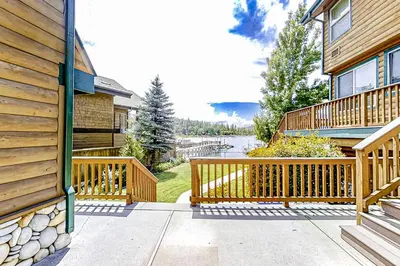 a house with a wooden porch with a lake in the background at Lakefront Retreat in Bass Lake