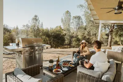a man and woman sitting on a patio with a grill at Sunset Glow Hidden Meadow BBQ HotTub by Casa Oso in Oakhurst
