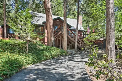 a large wooden house in the woods with a driveway at Comfortable Mi-Wuk Village Cabin Hike and Ski! in Mi-Wuk Village