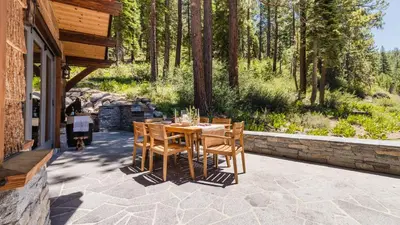 a wooden table and chairs on a patio with trees at Hunter by AvantStay Award-Winning Riverfront Cabin 5 Minutes from Palisades in Olympic Valley