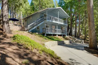 a blue house with a porch and balcony in the woods at 12 Mi to Apple Hill Family-Friendly Cabin Retreat in Pollock Pines