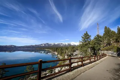 a wooden fence next to a lake with snow covered mountains at Take Me to Tahoe in Incline Village