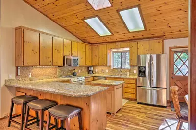 a kitchen with wooden cabinets and a large island with bar stools at Deck with Forest Views Quiet Twain Harte Cabin! in Twain Harte