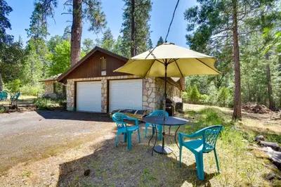 a table with chairs and an umbrella in front of a cabin at 7 Mi to Yosemite Natl Park Riverfront Getaway! in Groveland