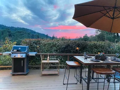 a wooden deck with a table and an umbrella at Cozy Cabin Near Yosemite & Bass lake, Breathtaking Views & Private Hot Tub, BBQ, Nature Getaway in Oakhurst