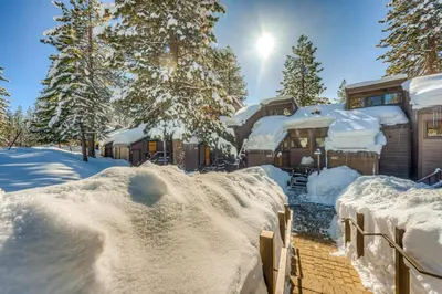 a house covered in snow with the sun in the background at The Pines at Rocky Point in Truckee