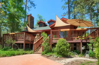 a large house with a large deck with an umbrella at Willow Cove Lodge- 5 bedrooms with a hot tub in Bass Lake