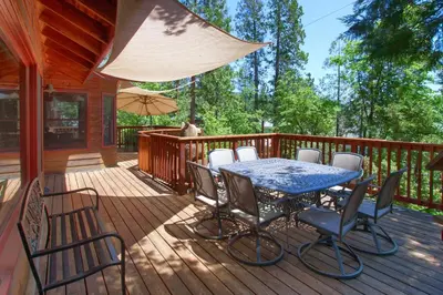 a deck with a table and chairs and an umbrella at Willow Cove Lodge- 5 bedrooms with a hot tub in Bass Lake