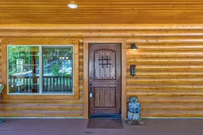 a wooden house with a door and a bear on the porch at Bass Lake Log Home - Dog Friendly in Bass Lake