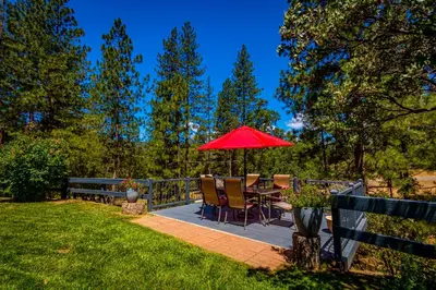 a patio with a table with a red umbrella at Starry Pines- Pet friendly/spa/affordable in Oakhurst