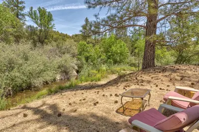 a table and chairs sitting on a hill next to a river at River View Retreat Sleeps 16/ hot tub/basketball court in Oakhurst