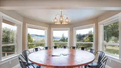a dining room with a table and chairs and windows at Yosemite Adventure House with Pool-hot tub-game room in Oakhurst