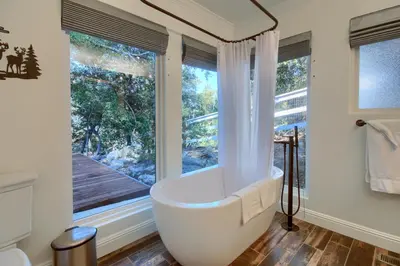 a bathroom with a tub and a large window at Doe Cabin Hot Tub/Playground/Game Room and more in Oakhurst