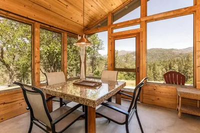 a dining room with a table and chairs and windows at Hilltop Haven- Bright and Modern Cabin w/ hot tub and stunning views in Oakhurst