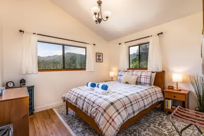 a bedroom with a bed and two windows at Hilltop Haven- Bright and Modern Cabin w/ hot tub and stunning views in Oakhurst