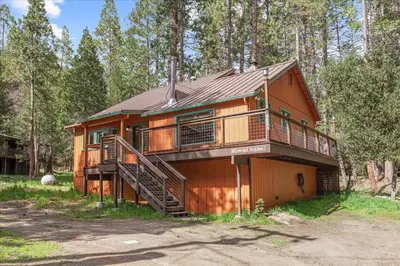 a large wooden house with a staircase in the woods at Cub House- Remodeled cabin INSIDE Yosemite with new hot tub and more in North Wawona