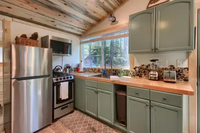 a kitchen with green cabinets and a stainless steel refrigerator at Beetlebark Bungalow- Inside Yosemite w/ hot tub EV charging cable in North Wawona