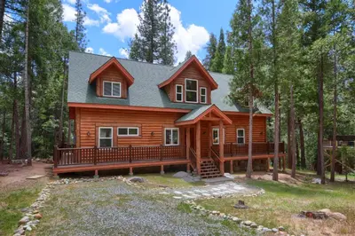 a log cabin in the woods with a large deck at Rivercrest Lodge with Hot Tub-Pool Table-Firepit in North Wawona