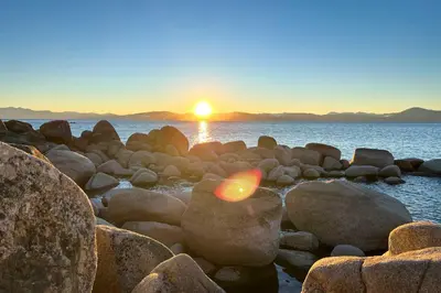 a sunset over the water with rocks on a beach at 1 Mi to Lake Tahoe Vacation Rental Home! in Stateline