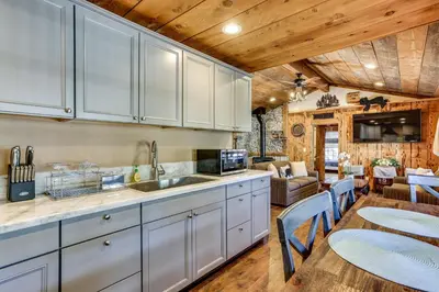 a kitchen with white cabinets and a living room at 9 Mi to Bass Lake Cabin with Fire Pit in Wishon! in Bass Lake Annex