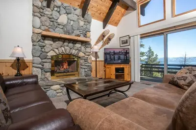 a living room with a stone fireplace and a table at Carnelian Bay View Cabin in Carnelian Bay