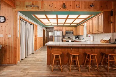 a kitchen with wooden cabinets and bar stools at Toste Cabin- Spacious 3BR Cabin in East Village! in Shaver Lake