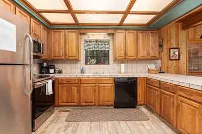 a kitchen with wooden cabinets and a black refrigerator at Toste Cabin- Spacious 3BR Cabin in East Village! in Shaver Lake