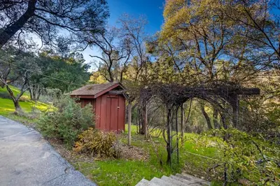 a red shed in the grass next to a road at Sierra Vista Lookout Lodge with Creek, Waterfall and Waterholes, minutes from Bass Lake and Yosemite South Gate in North Fork